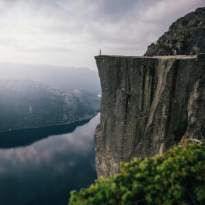 A lone adventurer stands on the edge of Preikestolen cliff, overlooking the stunning fjord below in Norway.
